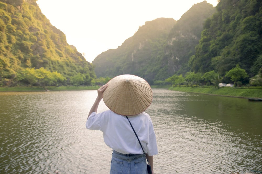 A serene moment as a girl in a traditional conical hat gazes across the tranquil lake 